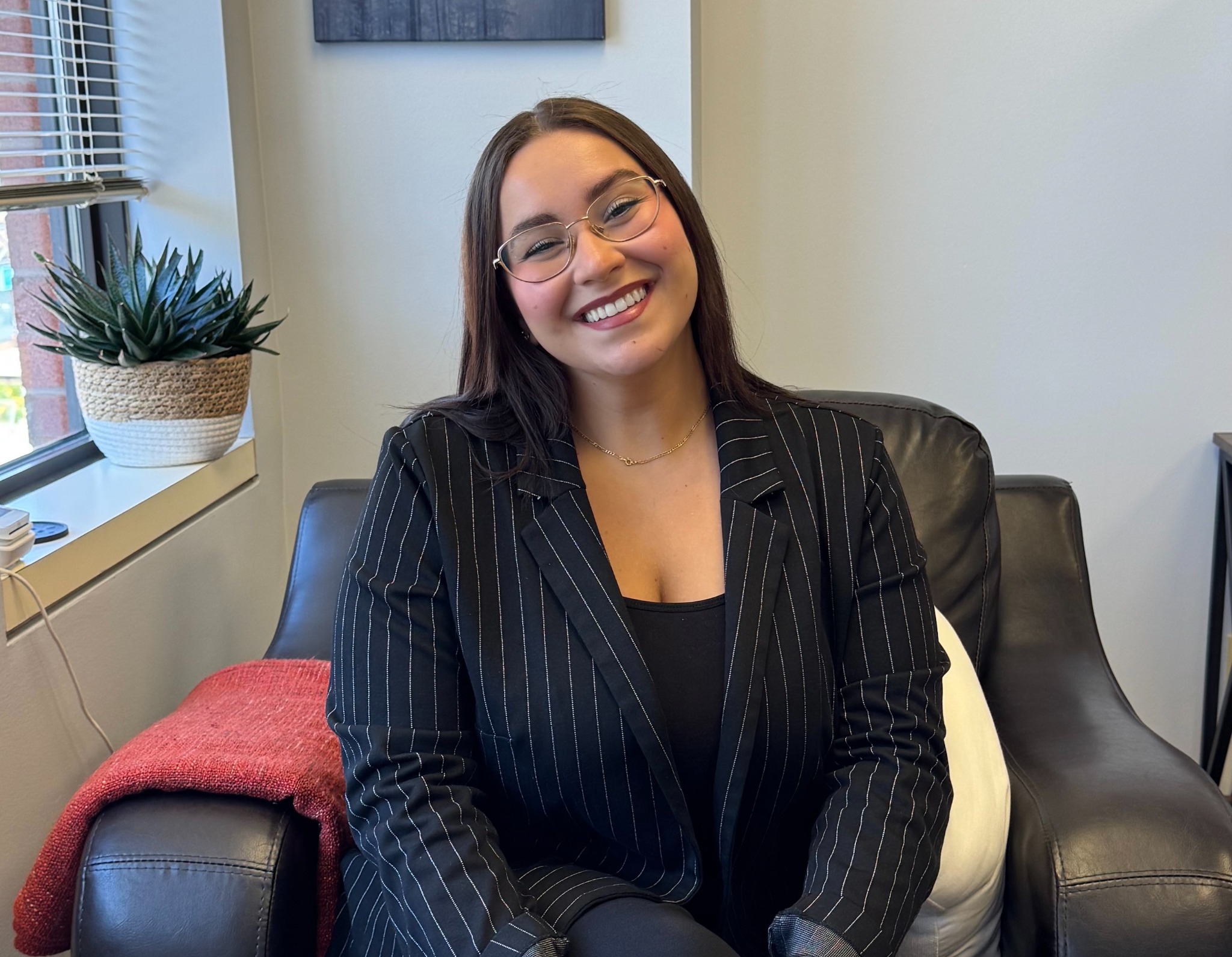 Amina Lazrak smiling in a black pinstripe jacket